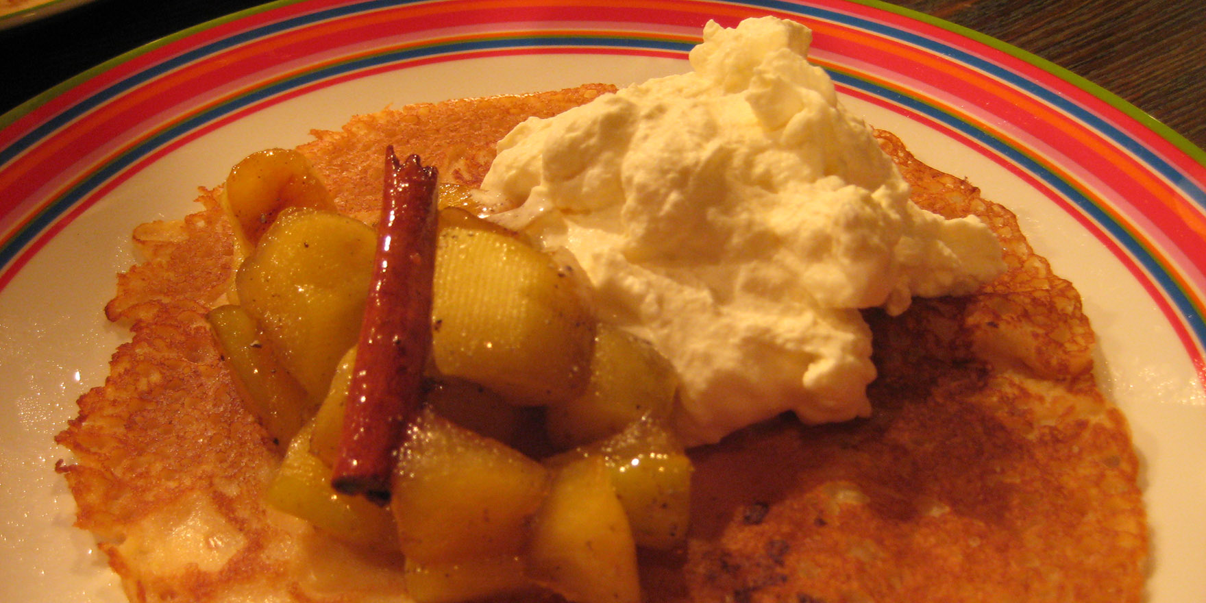 Lautasella pitsireunainen lettu, omenakuutiohilloketta, kanelitanko ja kermavaahtoa