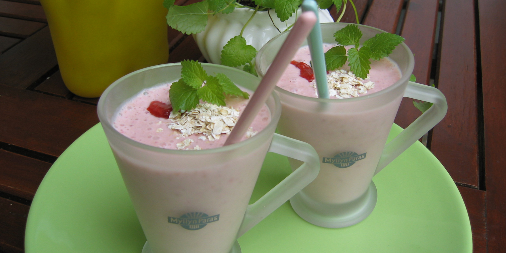 Kaksi lasimukia, joissa kaurasmoothieta, punaisia marjoja ja kaurahiutaleita pinnalla.