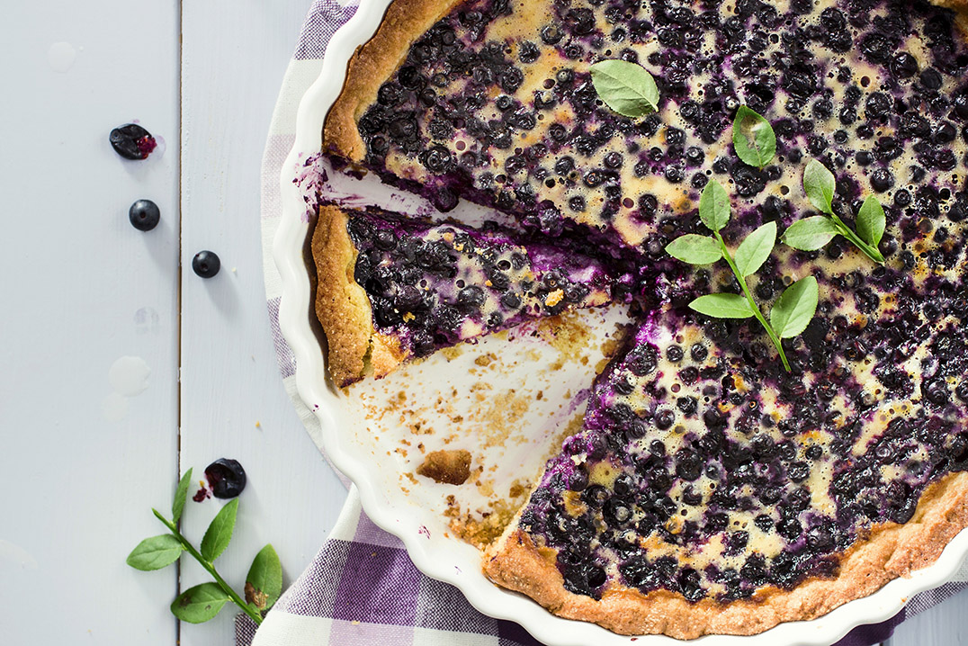 Pyöreä mustikkapiirakka, jossa pinnalla muruseosta ja mustikanvarpu koristeena.