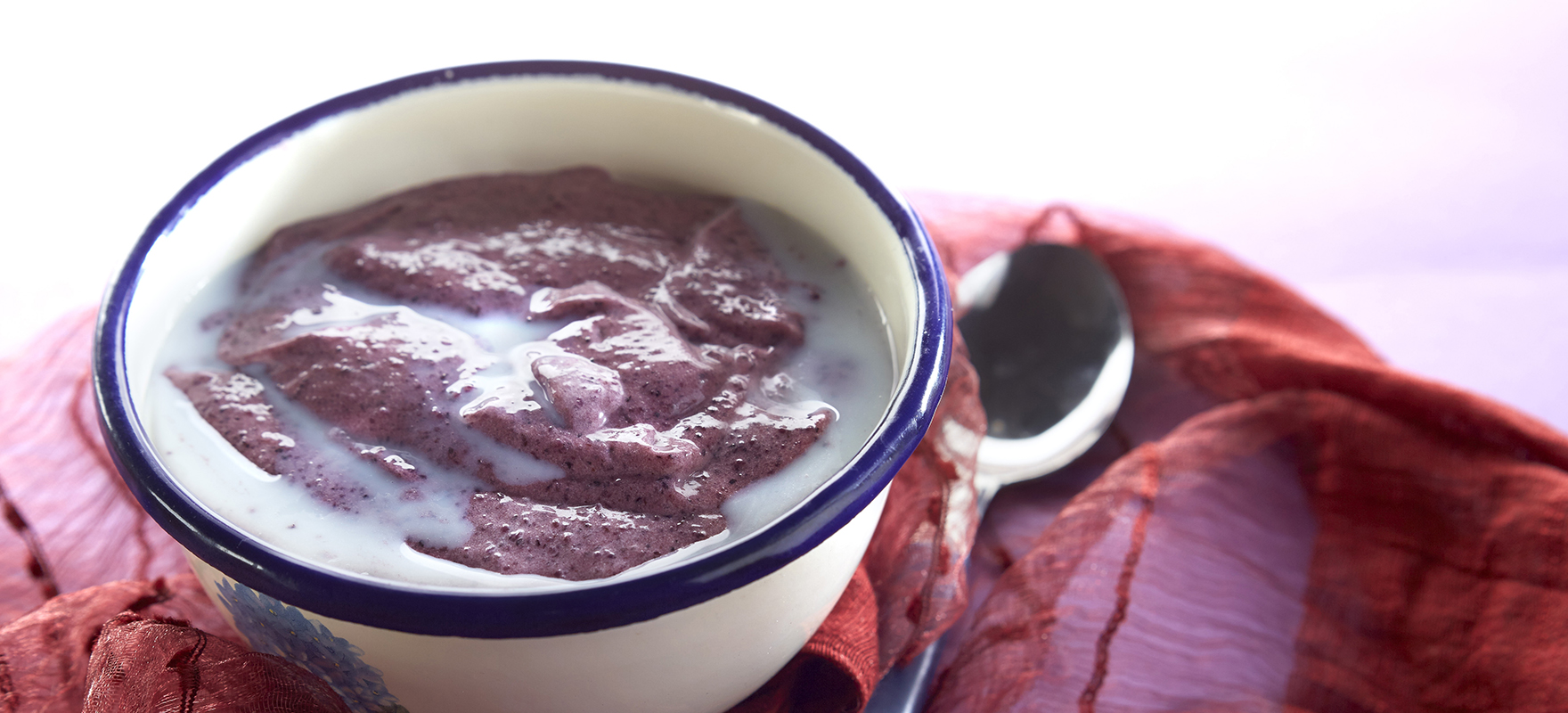 Punertavaa mustikkavispipuuroa lautasella maidon kera ja lusikka vieressä.