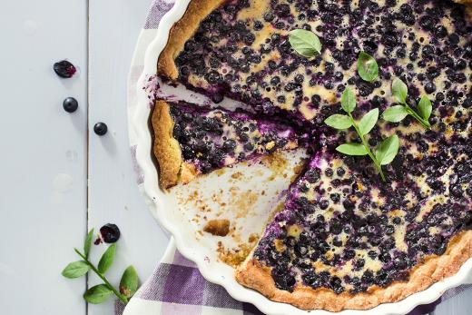 Pyöreä mustikkapiirakka, jossa pinnalla muruseosta ja mustikanvarpu koristeena.
