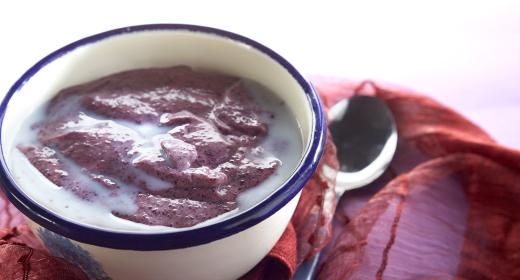 Punertavaa mustikkavispipuuroa lautasella maidon kera ja lusikka vieressä.