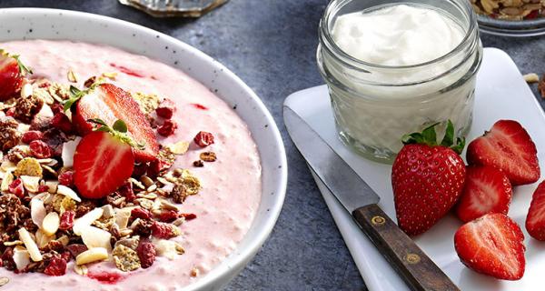 Lautasellinen jogurttia ja mysliä, mansikoita ja maitolasi.