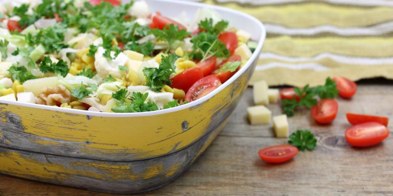 Salaattikulho jossa salaattia, pöydällä tomaatteja ja juustokuutioita