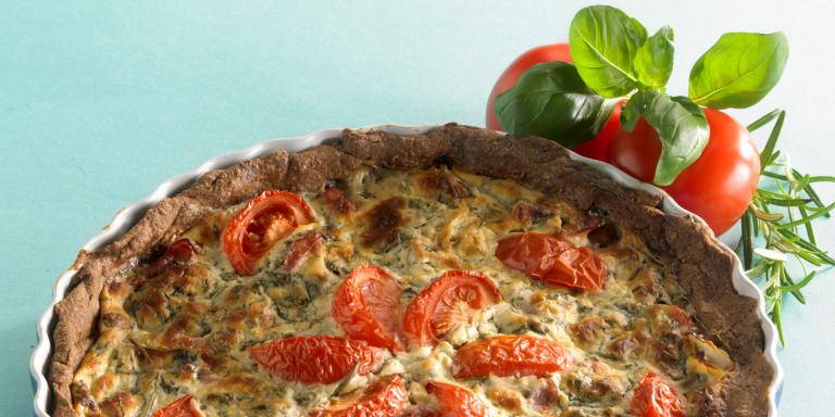 Pyöreä piirakkavuoka jossa kinkkua ja tomaattisuikaleita.