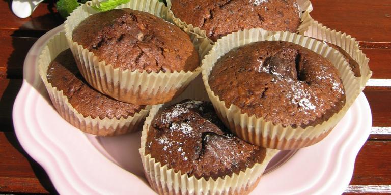 Lautasella kuusi paperimuotissa paistettua tummaa muffinia.