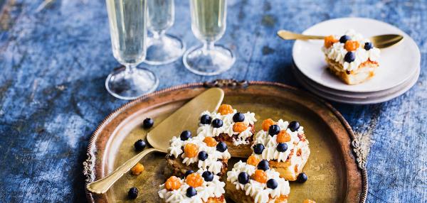 Mustikka-lakka koristellut leivokset tarjottimella sekä annos, 3 kuohuviinilasia