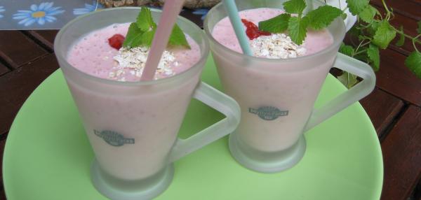 Vaaleanpunainen mustikkasmoothie tarjoiltuna kahdesta huurrelasisesta kahvikupista pilleineen, koristeltu punaisilla marjoilla, kaurahiutaleilla ja sitruunamelissan lehdillä.