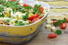 Salaattikulho jossa salaattia, pöydällä tomaatteja ja juustokuutioita