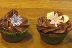 kaksi kuorrutettua ja kukalla koristeltua kuppikakkua paperimuoteissa