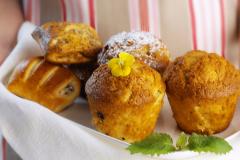 Kädet pitelevät tarjotinta jossa on vaaleita muffinsseja ja muita leivonnaisia