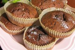 Lautasella kuusi paperimuotissa paistettua tummaa muffinia.