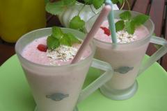 Kaksi lasimukia, joissa kaurasmoothieta, punaisia marjoja ja kaurahiutaleita pinnalla.