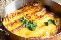 Pannulla juustokuorrutettuja, täytettyjä tortillaletturullia, pinnalla korianteria.